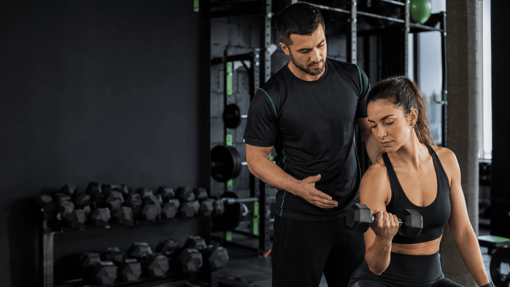 Entrenador personal en gimnasio: cómo funciona y cómo elegirlo en 2026 Entrenador personal corrigiendo la técnica de una clienta durante una sesión de fuerza en un gimnasio moderno